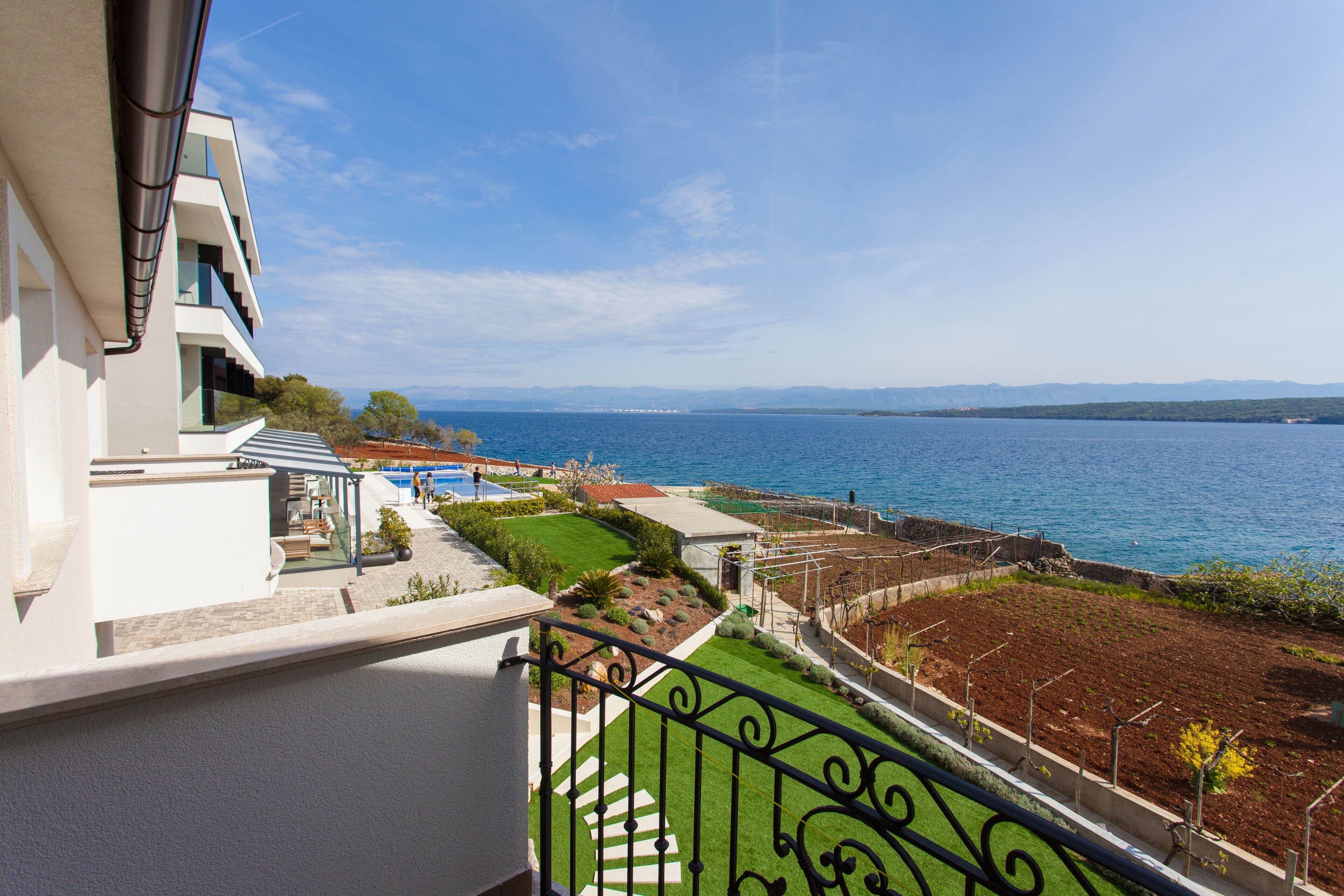 A balcony with a view of a pool, a garden, and a body of water.