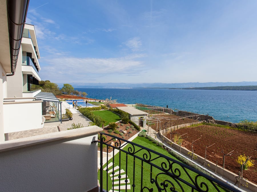 A balcony with a view of a pool, a garden, and a body of water.