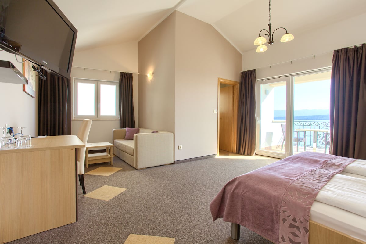 Ein Hotelzimmer mit Bett, Schreibtisch, Sessel, Sofa und einem Balkon mit Aussicht.
