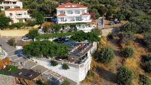 Un edificio de varios pisos con terraza en la azotea, rodeado de vegetación y automóviles estacionados.