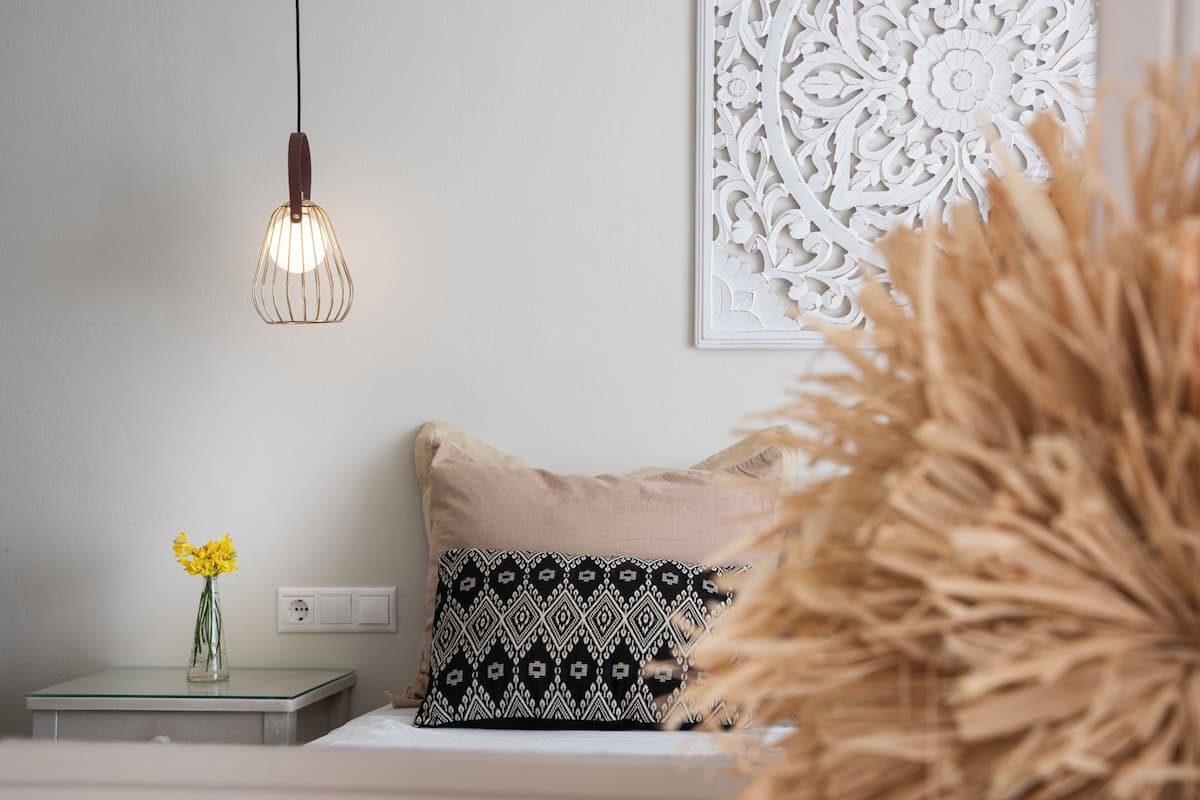 Une chambre avec une table de chevet, une lampe, un coussin à motifs et un élément décoratif mural.