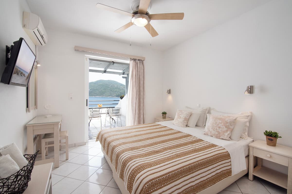 Une chambre à coucher comprenant un lit, des tables de chevet, un ventilateur de plafond, une télévision et une vue sur l’extérieur.