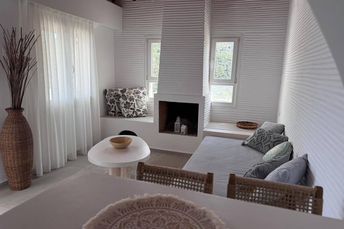 Un intérieur moderne avec une table ronde, des chaises en osier, une cheminée et un canapé agrémenté de coussins à motifs.