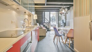 A modern kitchen with a central island, a dining area with chairs, and a staircase leading to an upper level. - Alcam Futbol (Barcelona)