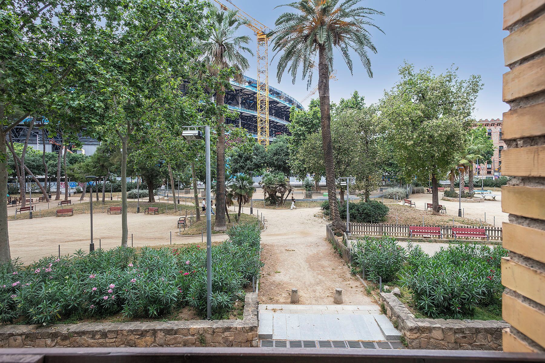 Un sendero que conduce a un parque con bancos, palmeras y una obra en construcción al fondo.