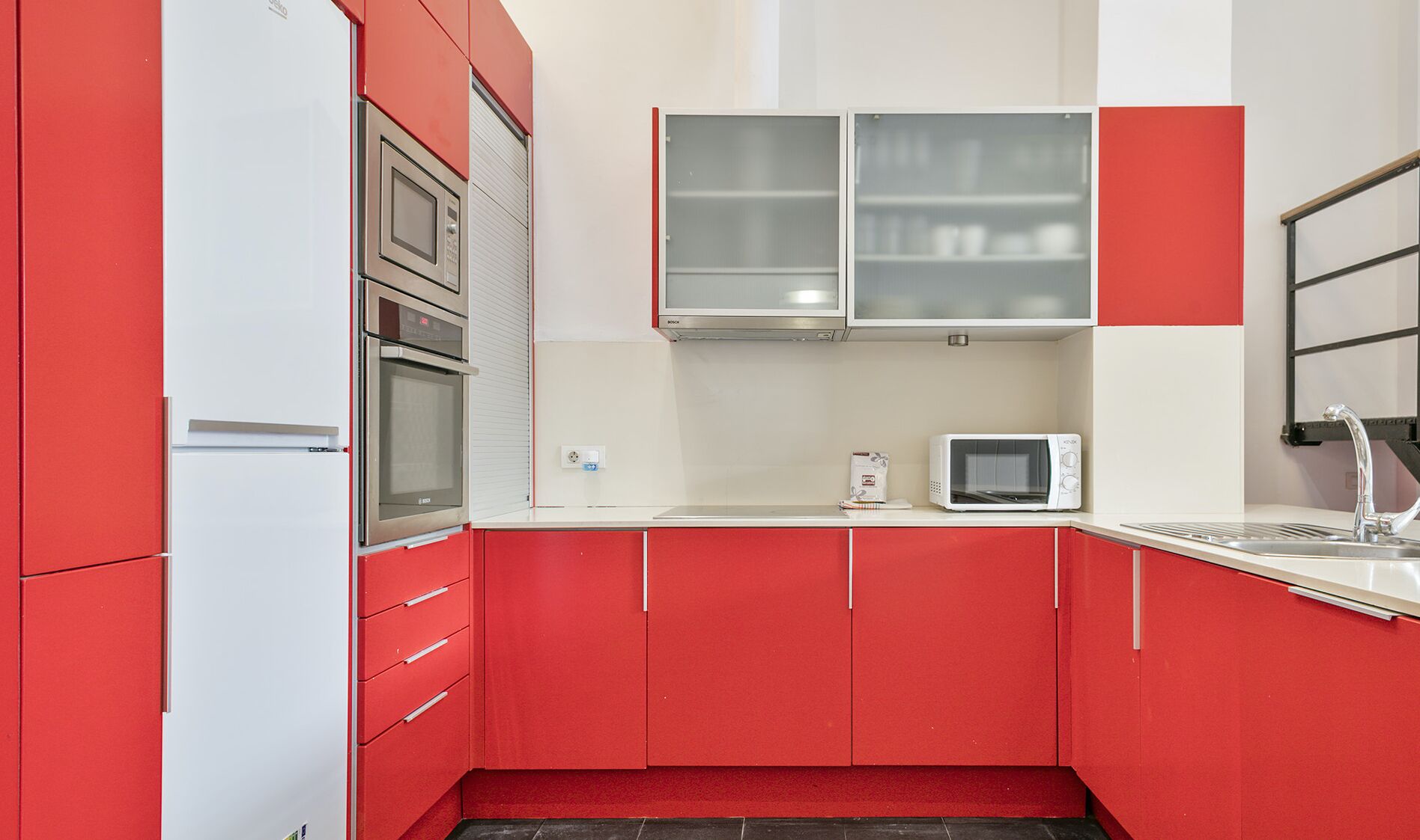 Una cocina compacta con gabinetes rojos, un refrigerador blanco, un microondas y un lavamanos.