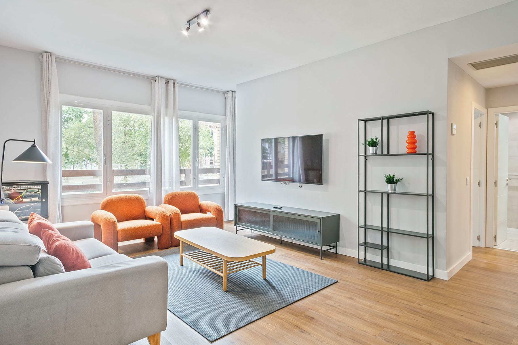 A modern living room with a sofa, chairs, a coffee table, a TV, and a bookshelf.