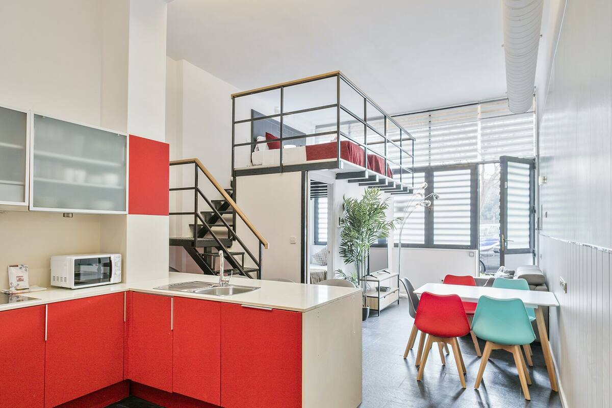 A compact kitchen with red cabinets, a microwave, and a sink. A staircase leads to a dining area with a table and chairs.
