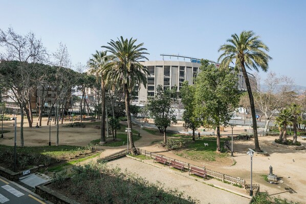 A park with palm trees, benches, and a building in the background. - Alcam Futbol (Barcelona)