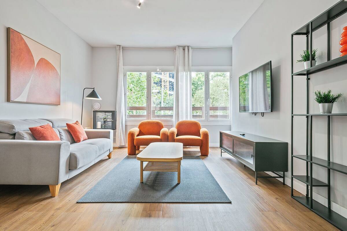 A modern living room with a sofa, two armchairs, a coffee table, a TV, and a bookshelf.