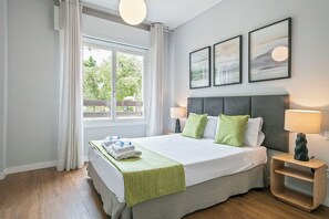 A neatly made bed with pillows, a bedside table with a lamp, and a window with curtains. - Alcam Futbol (Barcelona)