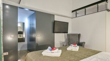Habitación de hotel con cama, una silla, televisor y baño visible a través de una puerta abierta.