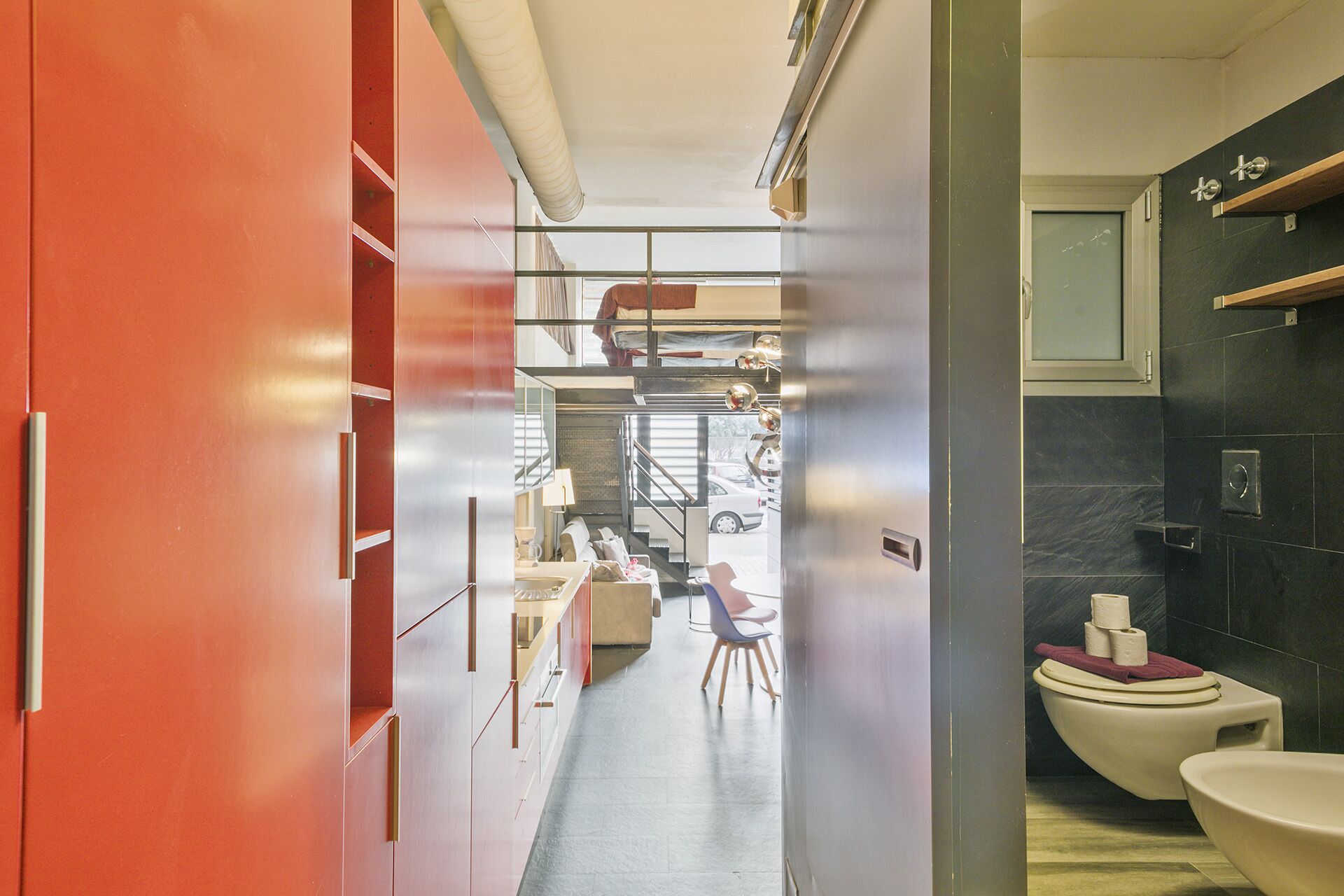 A modern hotel room with a compact layout, including a small seating area, a kitchenette, and a bathroom with a toilet and sink.