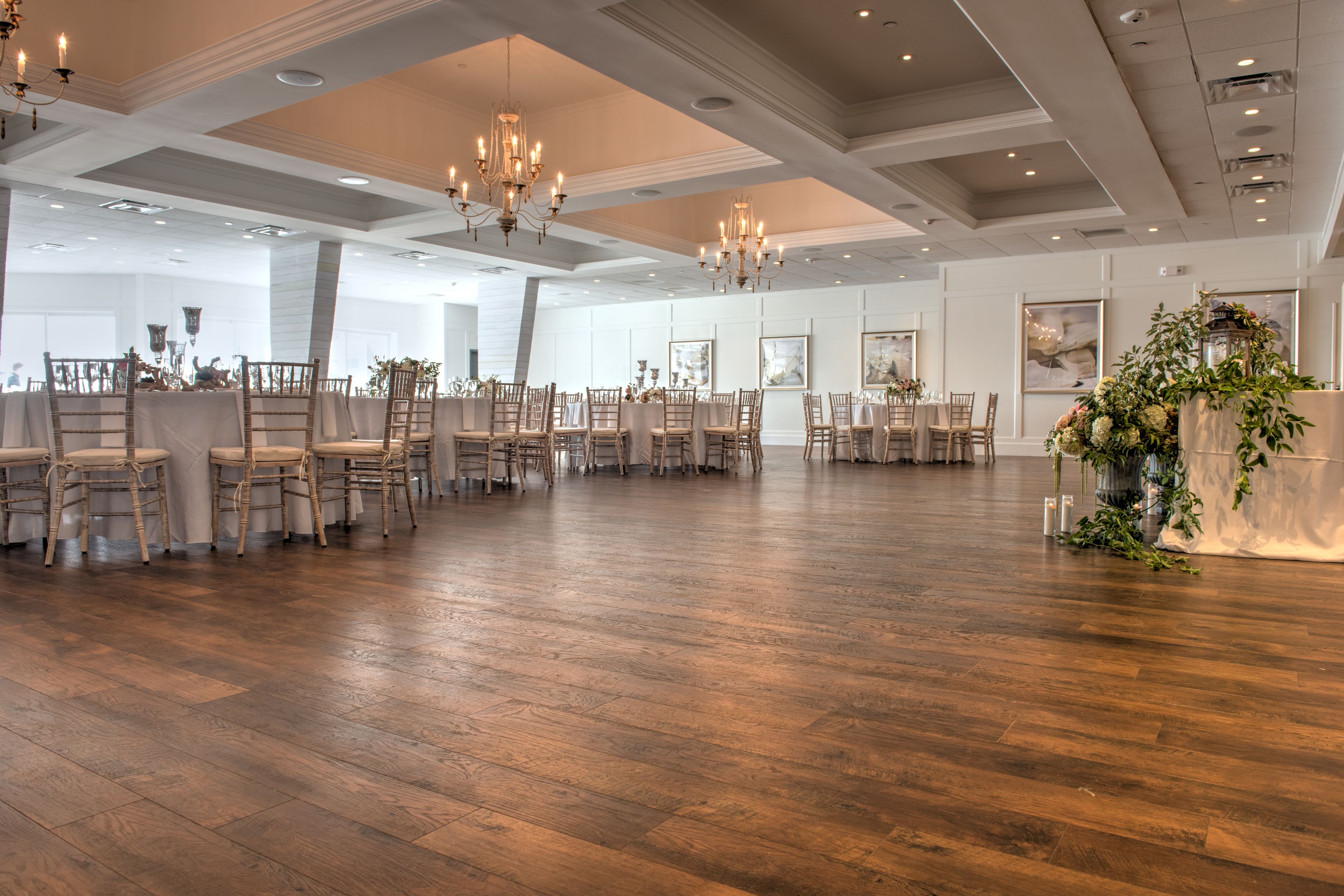 A spacious hall with wooden flooring, arranged seating, and decorative chandeliers.