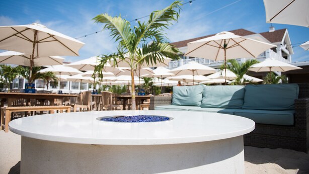 An outdoor seating area with round tables, white umbrellas, and a palm tree.