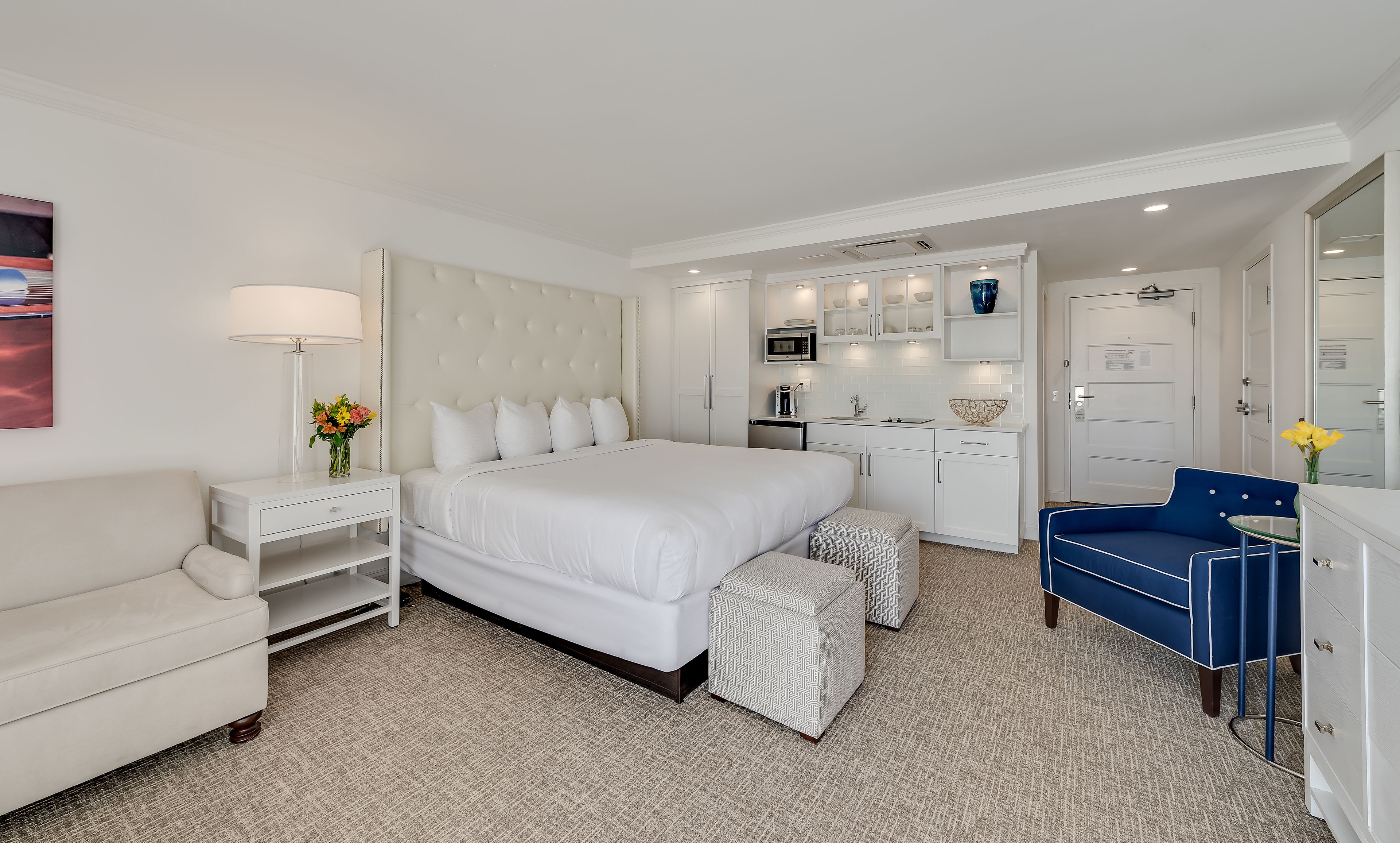 A hotel room with a large bed, a desk, a chair, a small table, and a bathroom area.
