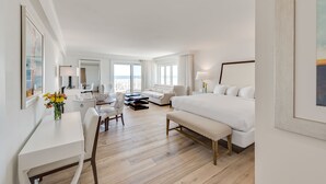 A hotel room with a large bed, a sitting area with a sofa and chairs, a dining table, and a view of the ocean.