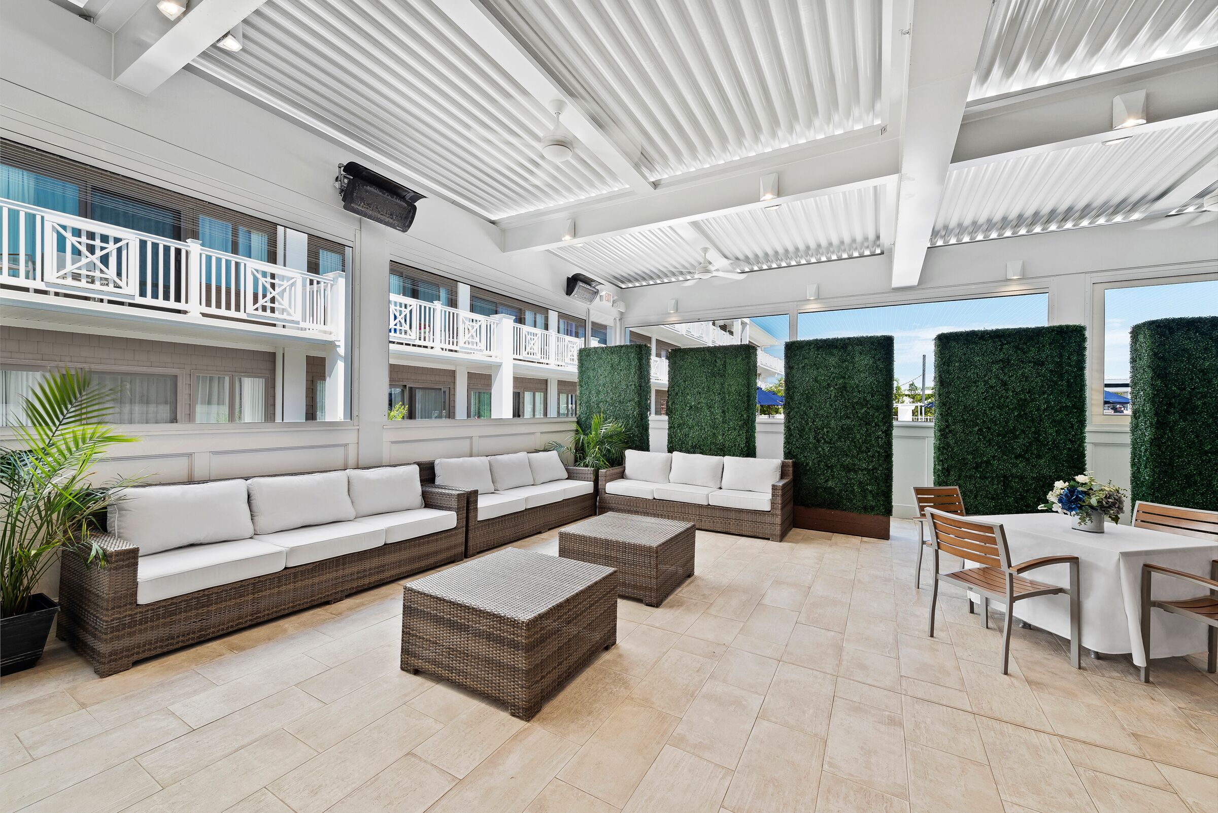 A spacious outdoor lounge area with wicker furniture, white cushions, and a dining table set for four.