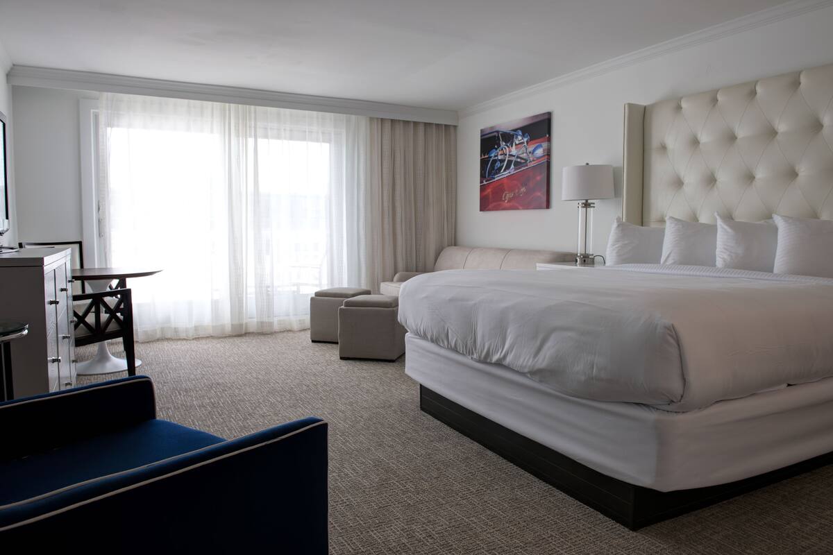 Une chambre d’hôtel avec un grand lit, un bureau, une chaise et une fenêtre avec des rideaux.
