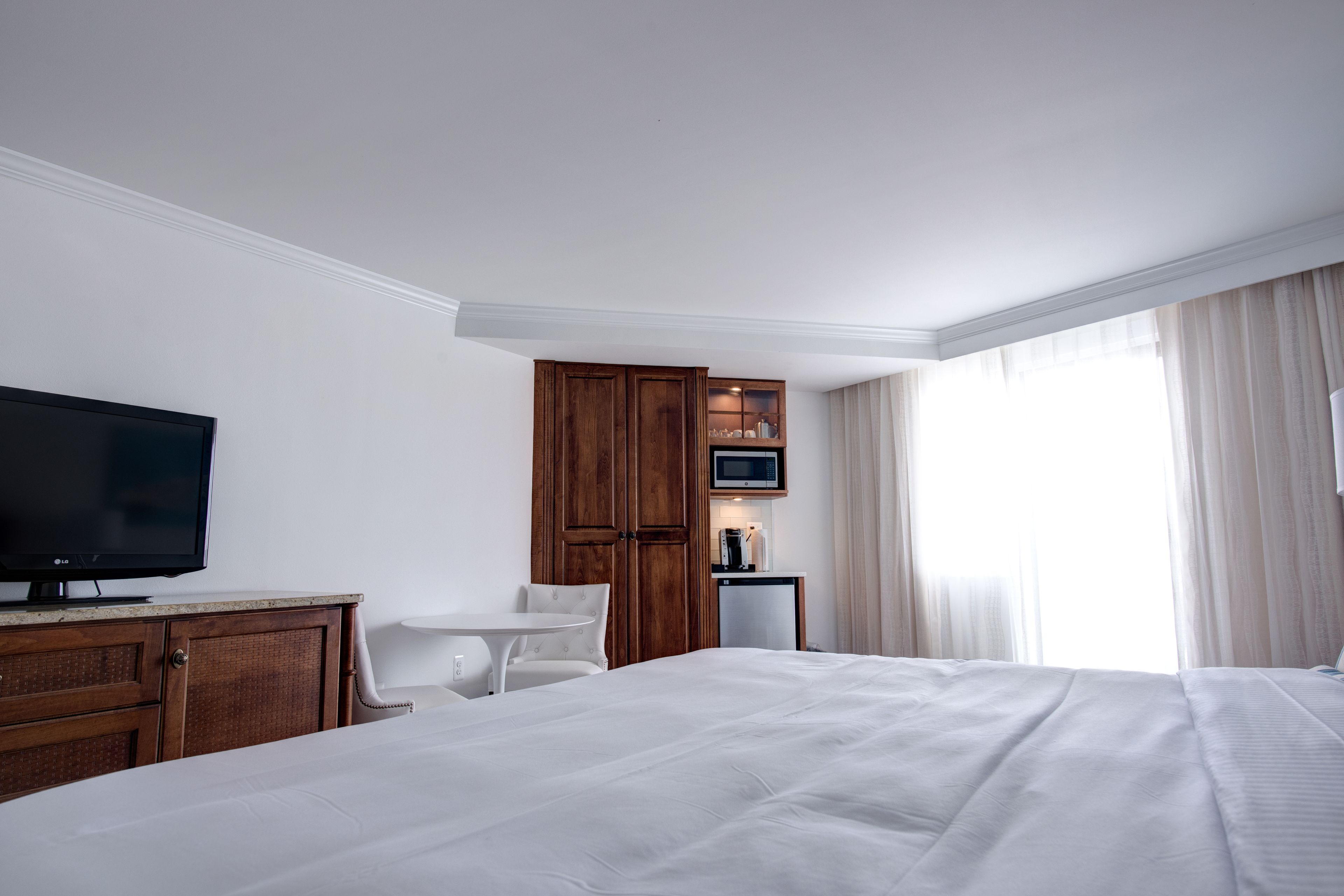 A hotel room with a large bed, a television, a wooden wardrobe, a small table, and a window with curtains.