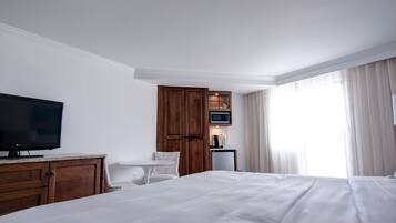 A hotel room with a large bed, a television, a wooden wardrobe, a small table, and a window with curtains.