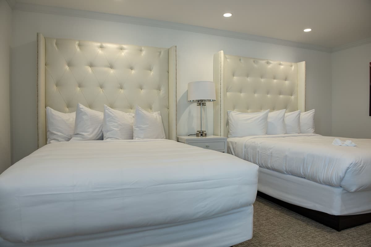 Une chambre d’hôtel avec deux lits, chacun doté d’une tête de lit capitonnée et de linge de lit blanc.