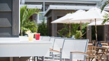 Een patio met witte tafels en stoelen, parasols en tropische planten.