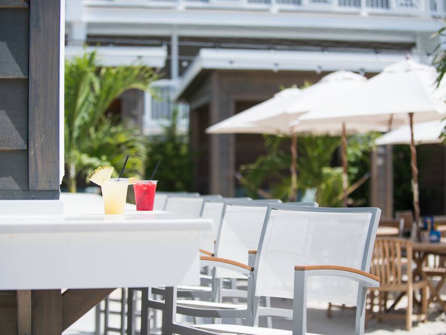 Een patio met witte tafels en stoelen, parasols en tropische planten.