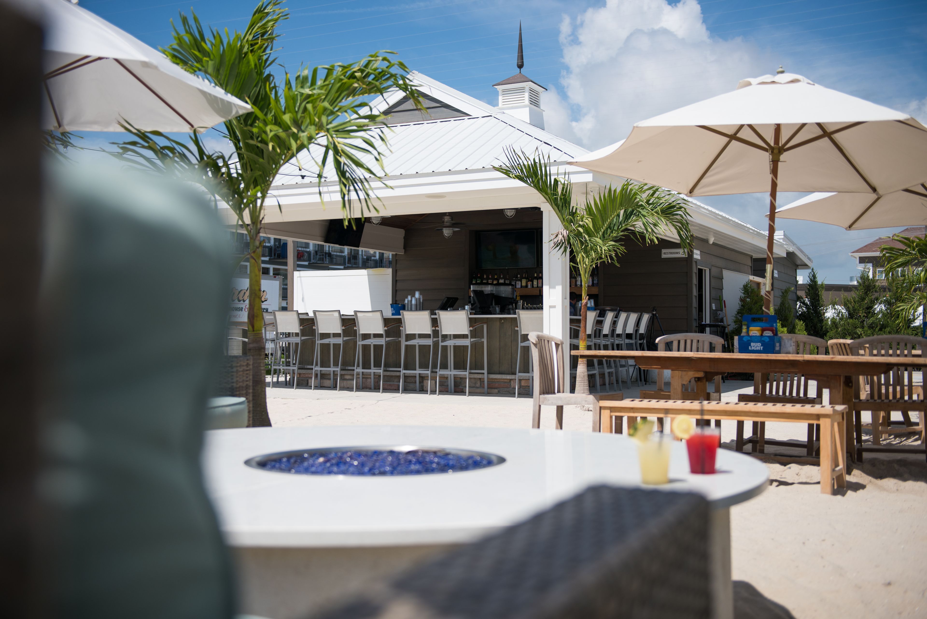 An outdoor seating area with tables and umbrellas, a pool, and a building with a white facade and a chimney.