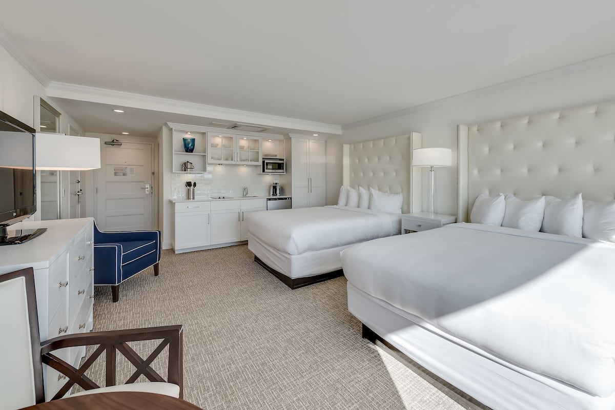 Une chambre d’hôtel avec deux lits, un bureau, une chaise, une télévision et une kitchenette.
