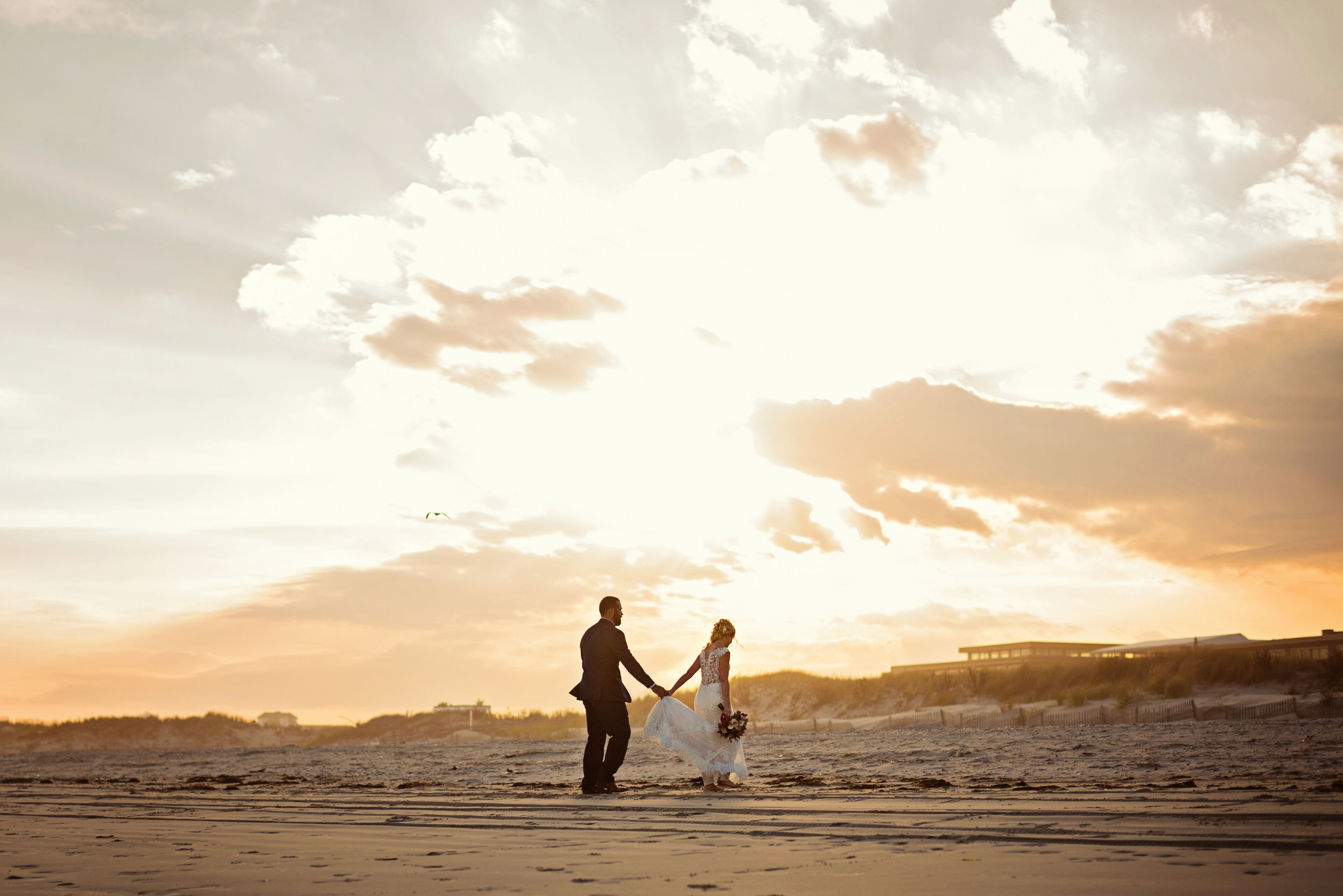 A couple holding hands on a beach at sunset.