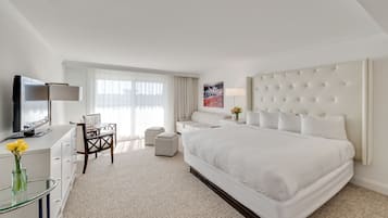 A modern hotel room with a large bed, a flat-screen TV, a desk with a chair, and a window with sheer curtains.