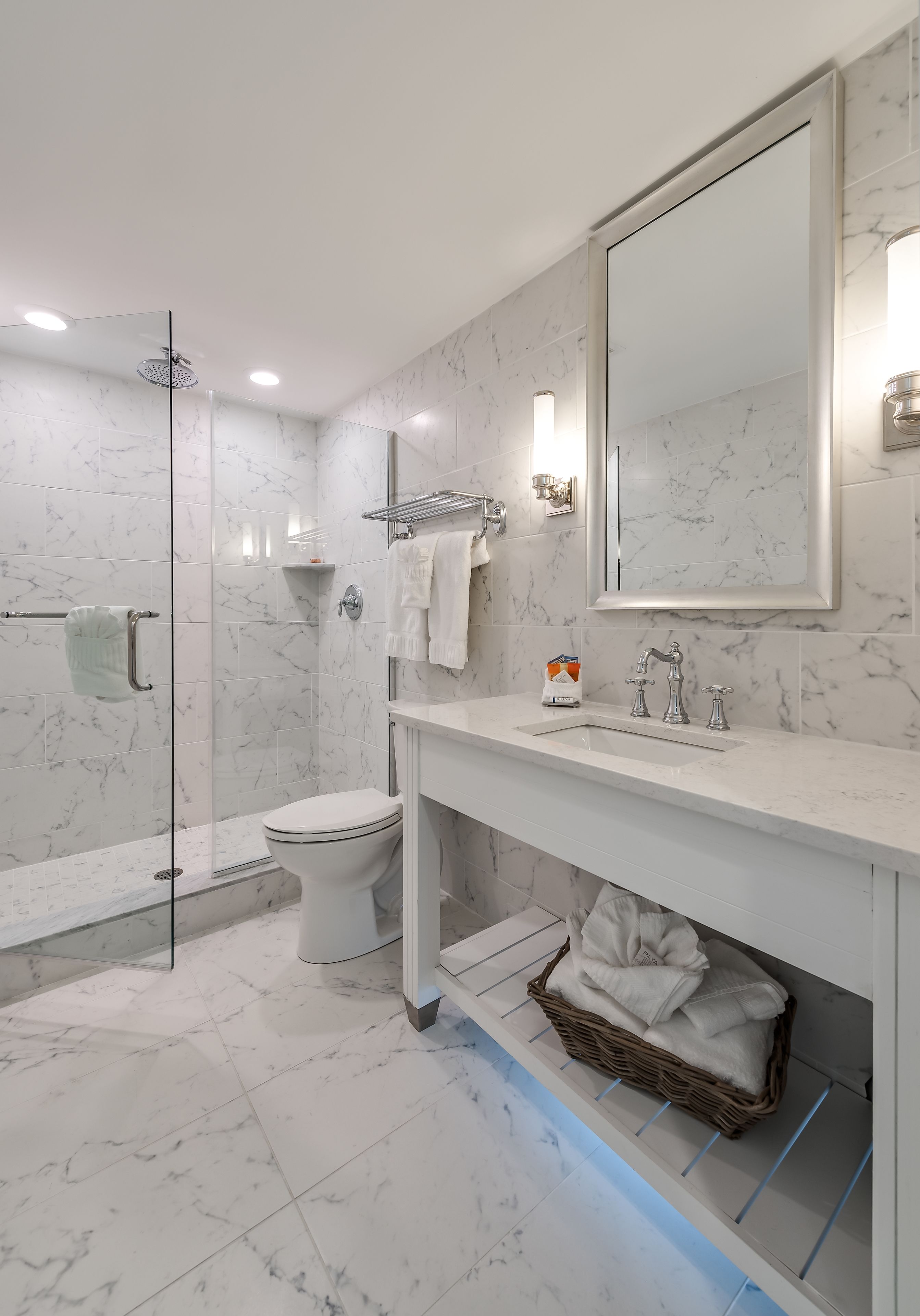 A modern bathroom with a glass shower enclosure, a white toilet, and a marble-tiled floor.