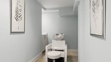 Un couloir étroit avec des toilettes blanches, un lavabo et une œuvre d’art représentant une feuille, encadrée, accrochée aux murs.
