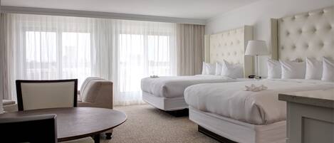 A hotel room with two beds, a dining table, and a chair.