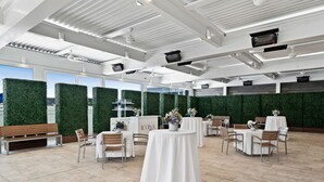 A spacious indoor area with high ceilings, green wall accents, and multiple tables and chairs arranged for dining or events.