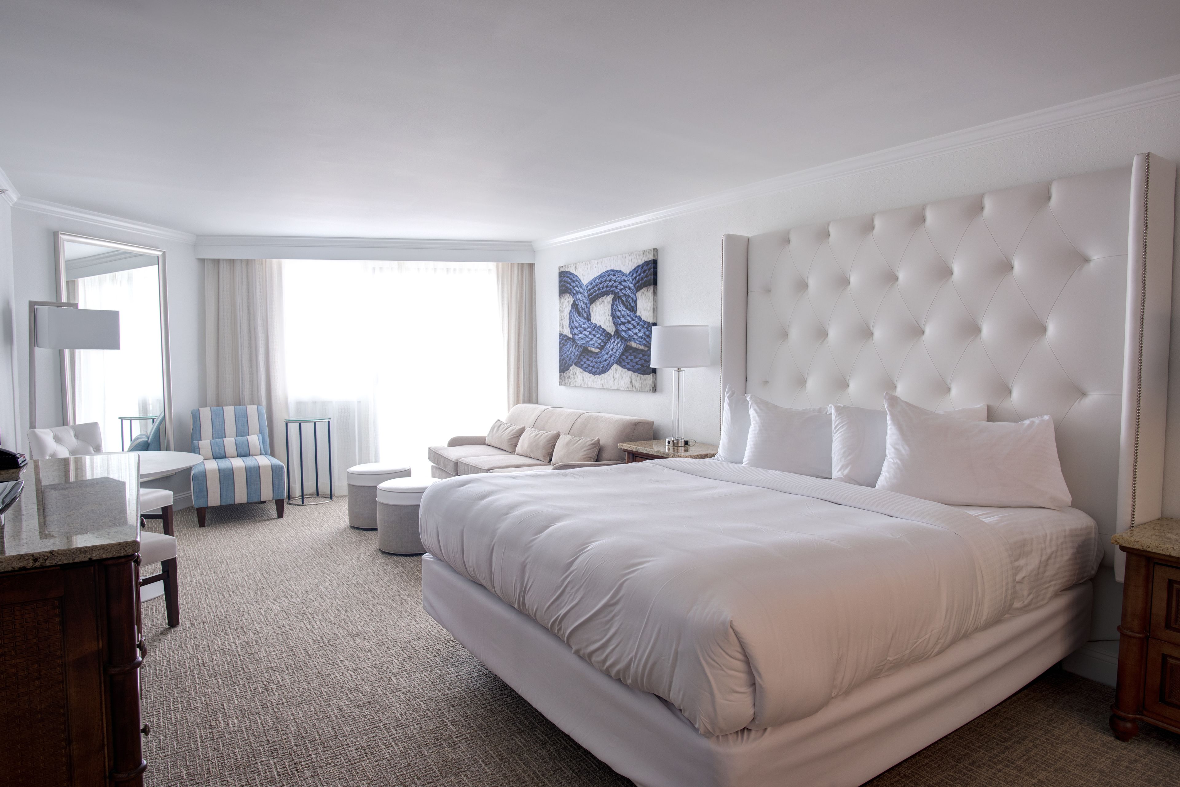 Een hotelkamer met een groot bed, een bureau met stoel, een bank en een groot raam.
