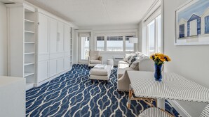 Amplia habitación con alfombra estampada, muebles blancos y un gran ventanal con vistas al mar.