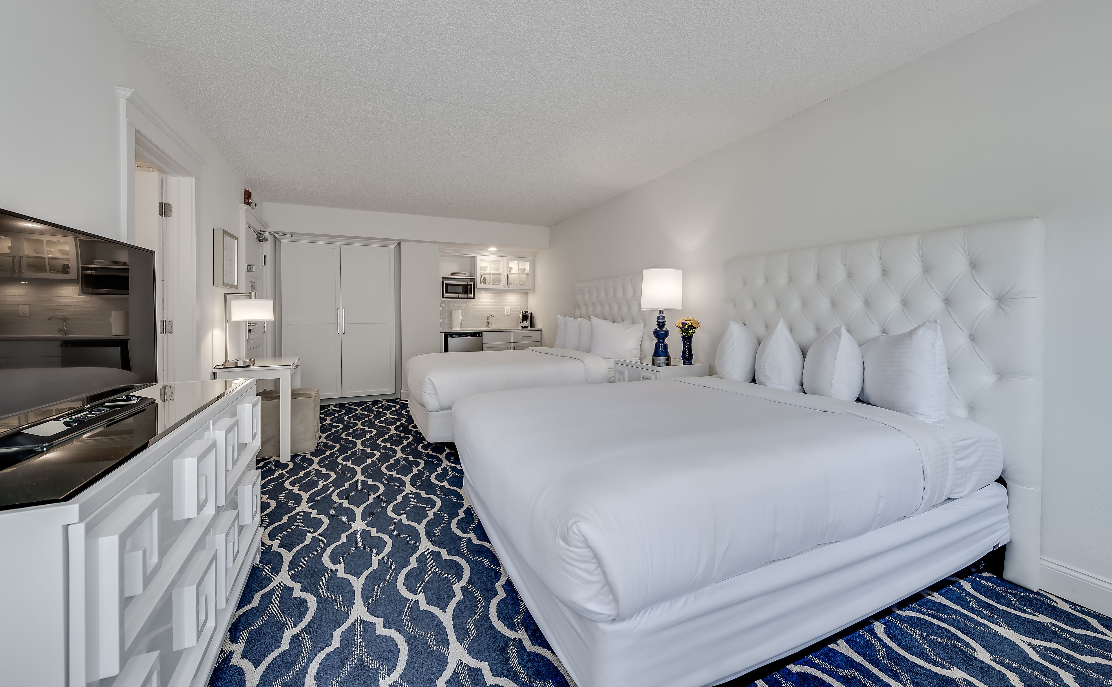 A hotel room with a large bed, a desk with a TV, a kitchenette, and a bathroom.