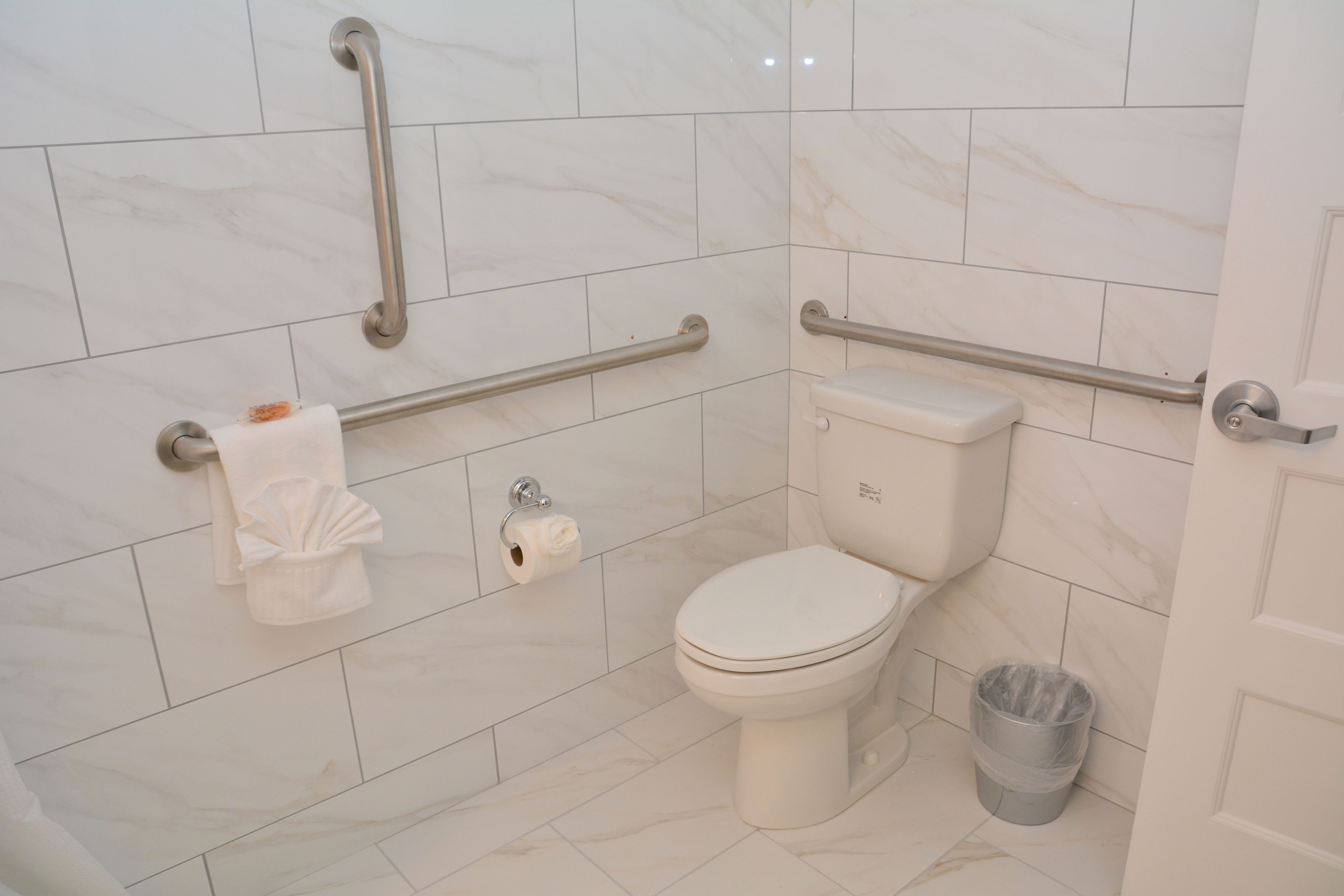 A bathroom with a toilet, grab bars, a trash can, and a towel rack.