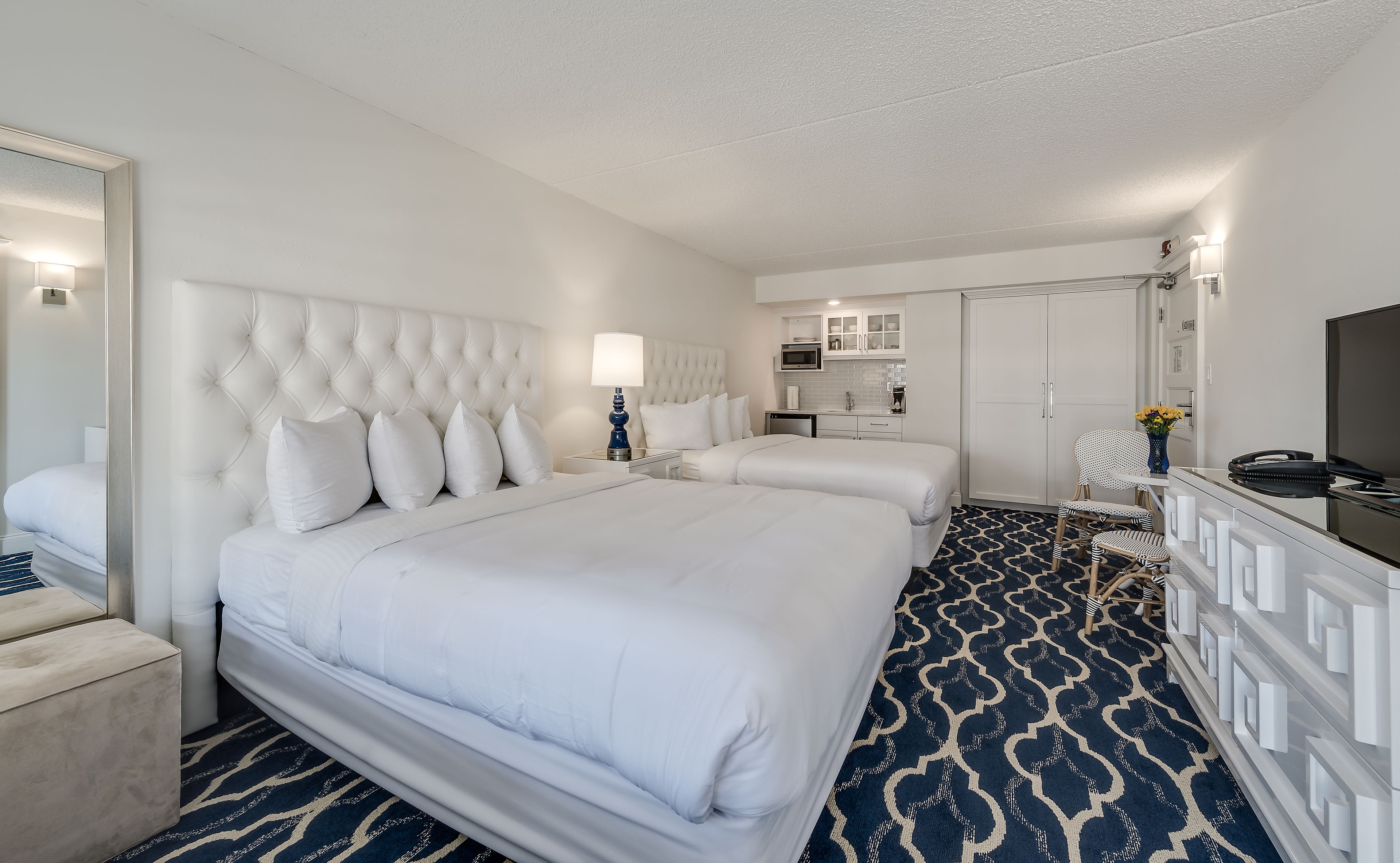 A hotel room with a large bed, a smaller bed, a desk, a chair, a TV, and a wardrobe.