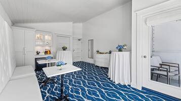 Una habitación blanca con alfombra azul estampada, muebles blancos y una mesa con flores.