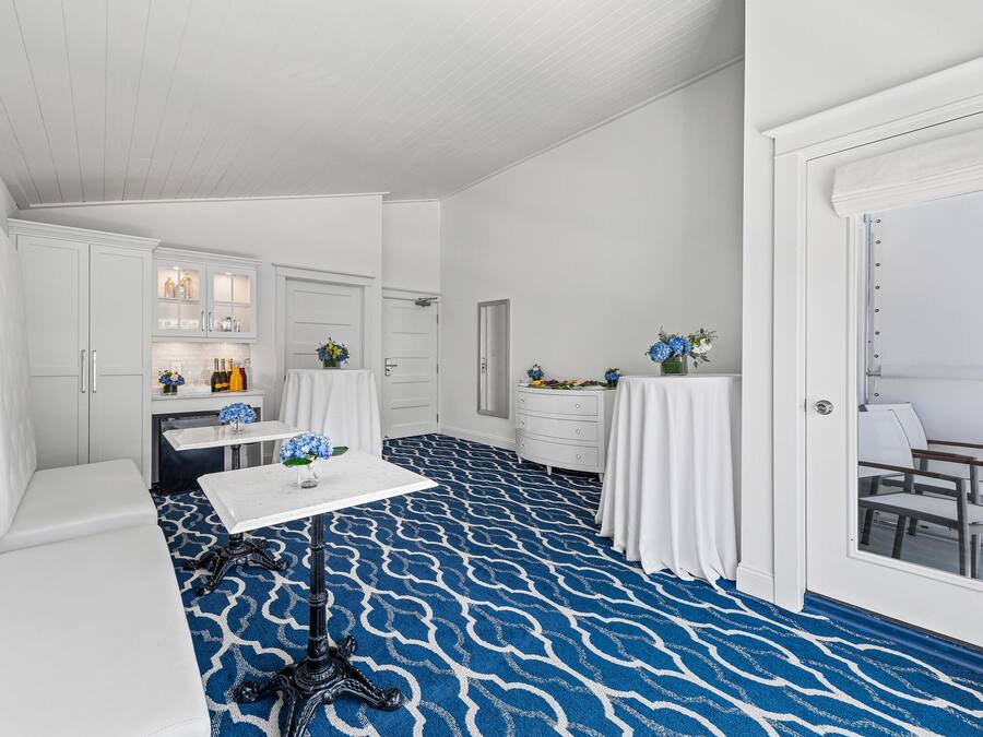 Una habitación blanca con alfombra azul estampada, muebles blancos y una mesa con flores.