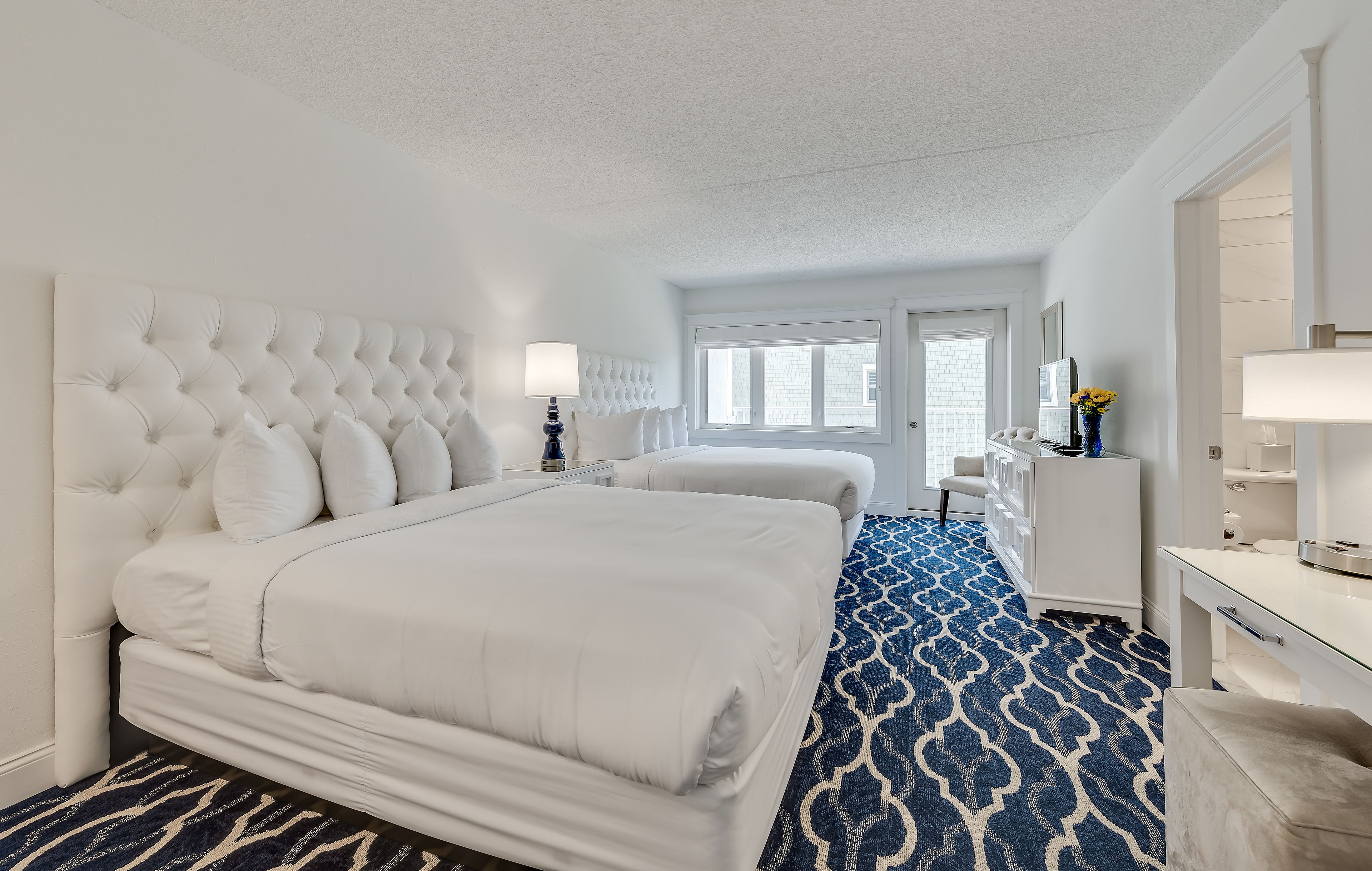 A hotel room with a large bed, a dresser, a vanity, and a window with a view of the city.