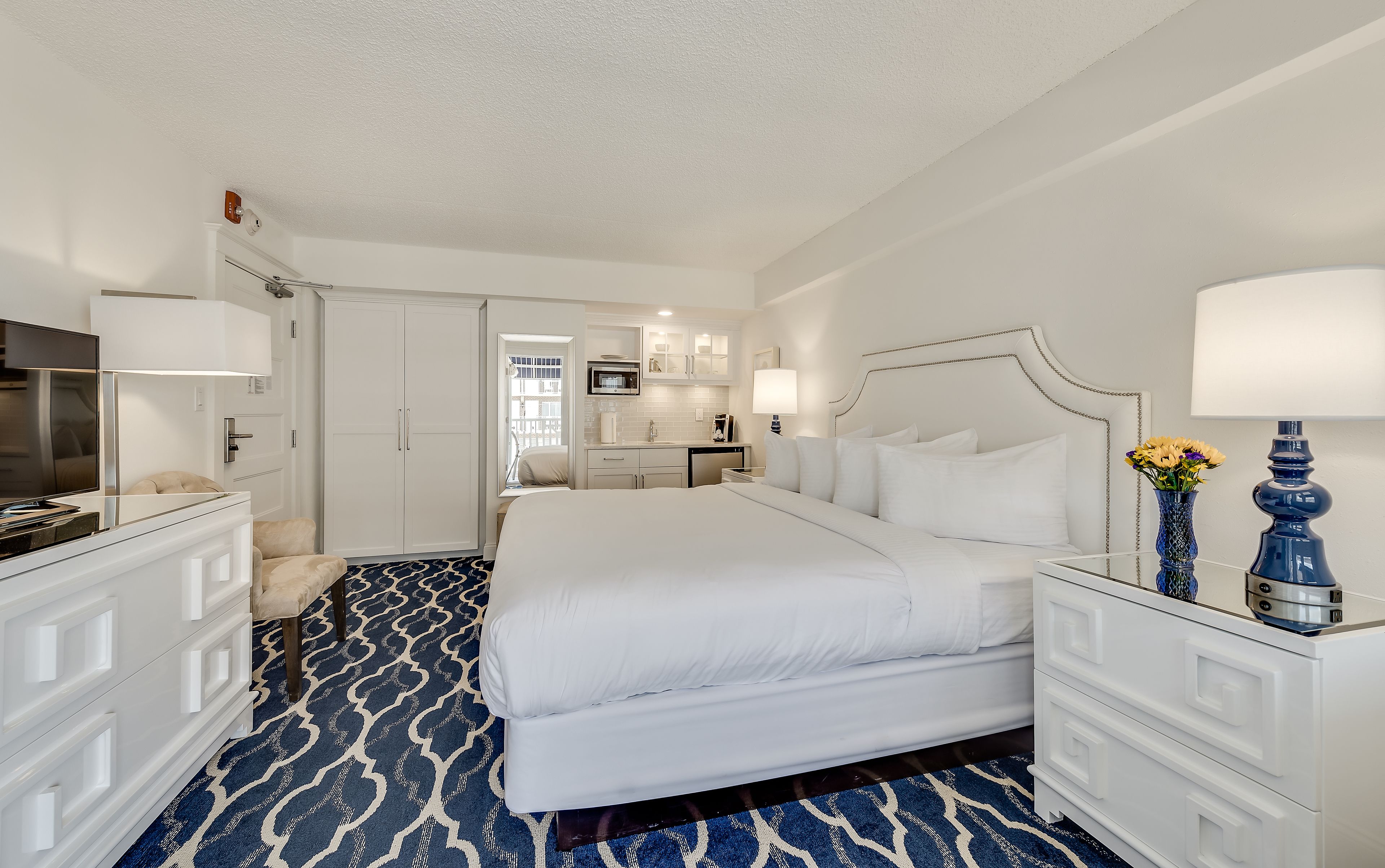 Une chambre d’hôtel avec un grand lit, un bureau, une chaise, une télévision et une salle de bain visible à travers une porte ouverte.