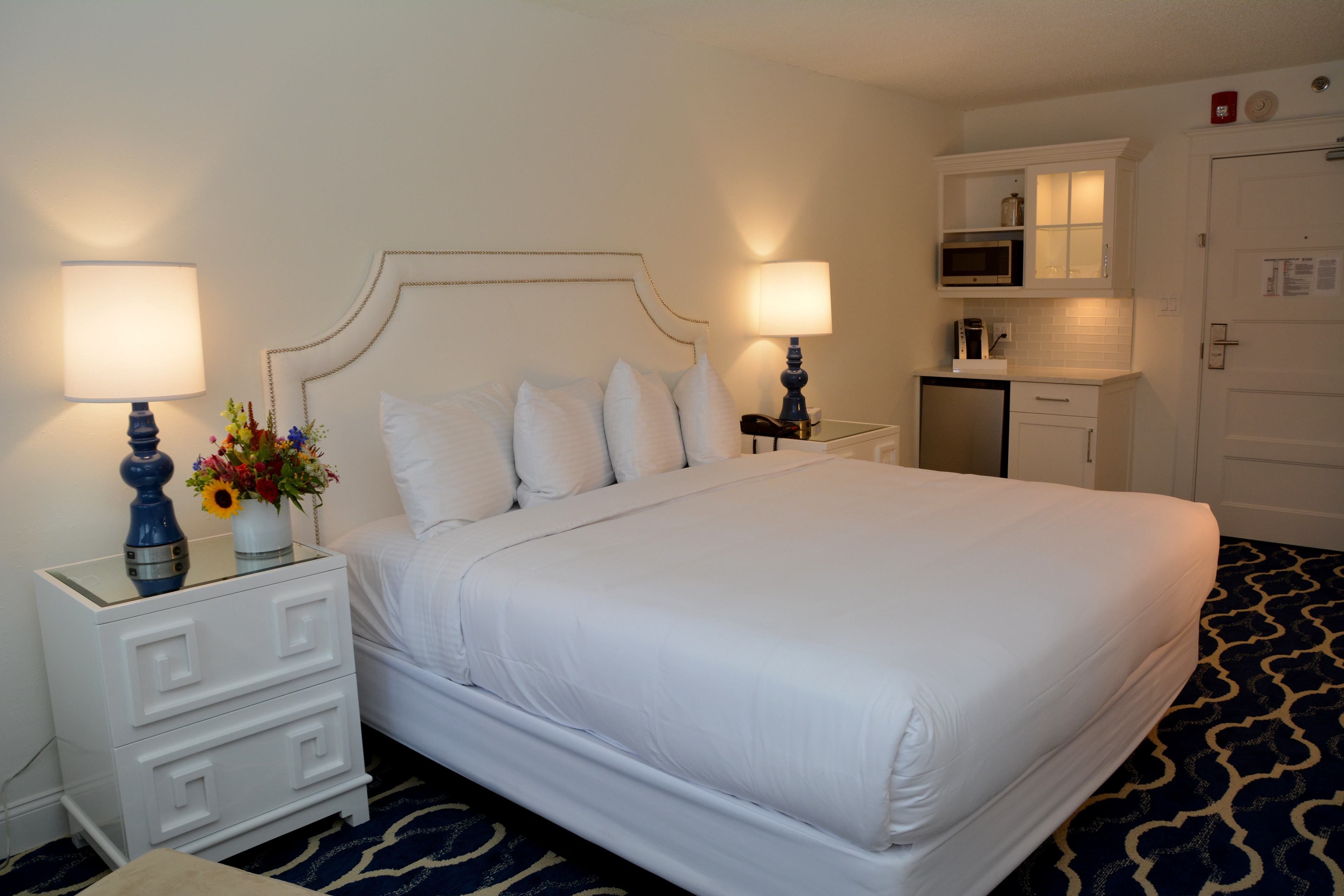 Habitación de hotel con una cama grande, dos mesitas de noche con lámparas, un escritorio pequeño, un microondas y un refrigerador.