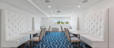 A conference room with white upholstered headboards, a blue patterned carpet, and a view of the outdoors through large windows.