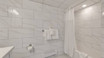 A modern bathroom with white marble tiles, a glass shower enclosure, and a toilet with a paper towel dispenser.