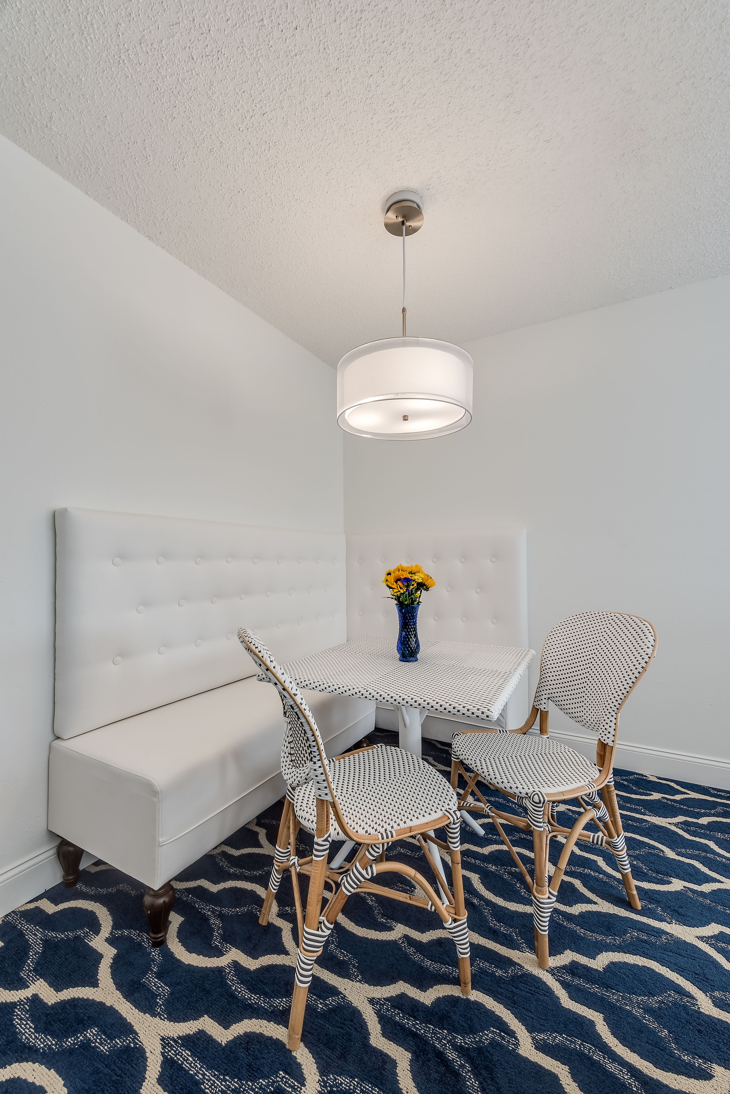 A room with a white sofa, a round table with two chairs, a vase with flowers, and a patterned rug.
