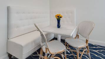 A room with a white sofa, a round table with two chairs, a vase with flowers, and a patterned rug.